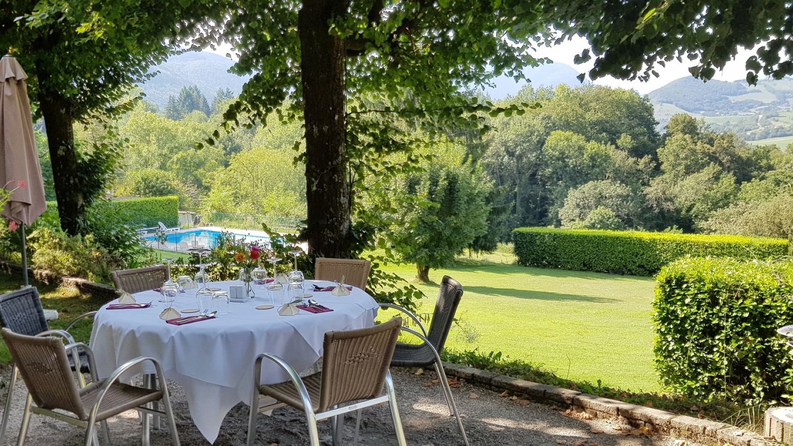 Terrasse ensoleillée table ronde, recouverte d'une nappe, chaises en osier, aux textures douces et légèrement courbées.