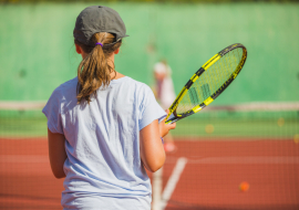 photo d'une jeune de dos tenant une raquette de tennis