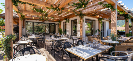 terrasse avec tables dressées sous pergolas en bois et végétaux