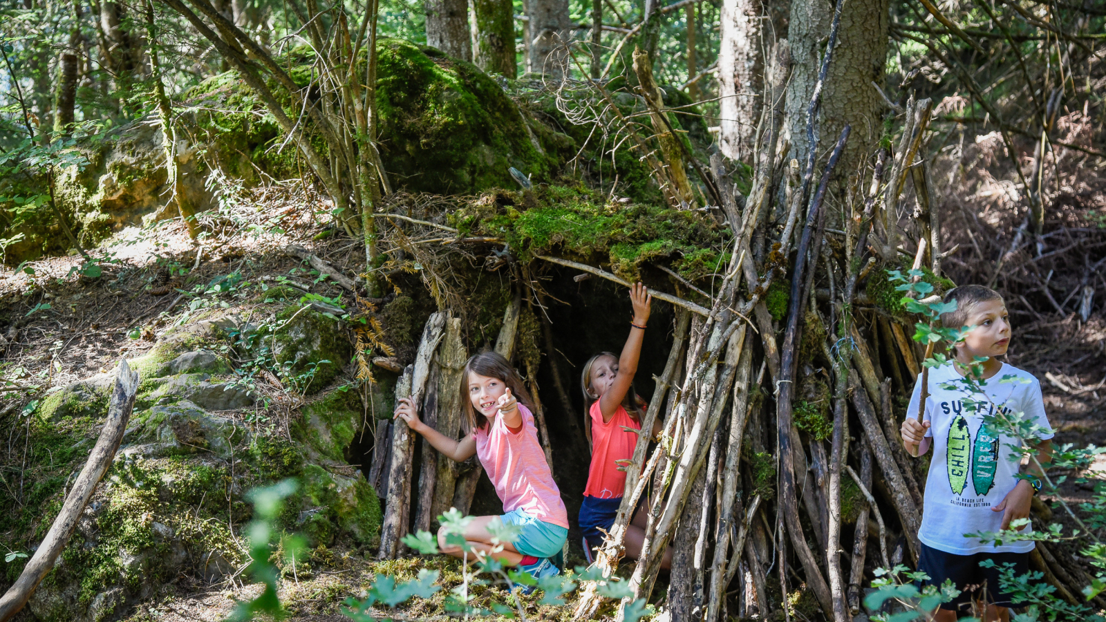 3 enfants en train de construire une cabane avec des branches d'arbre