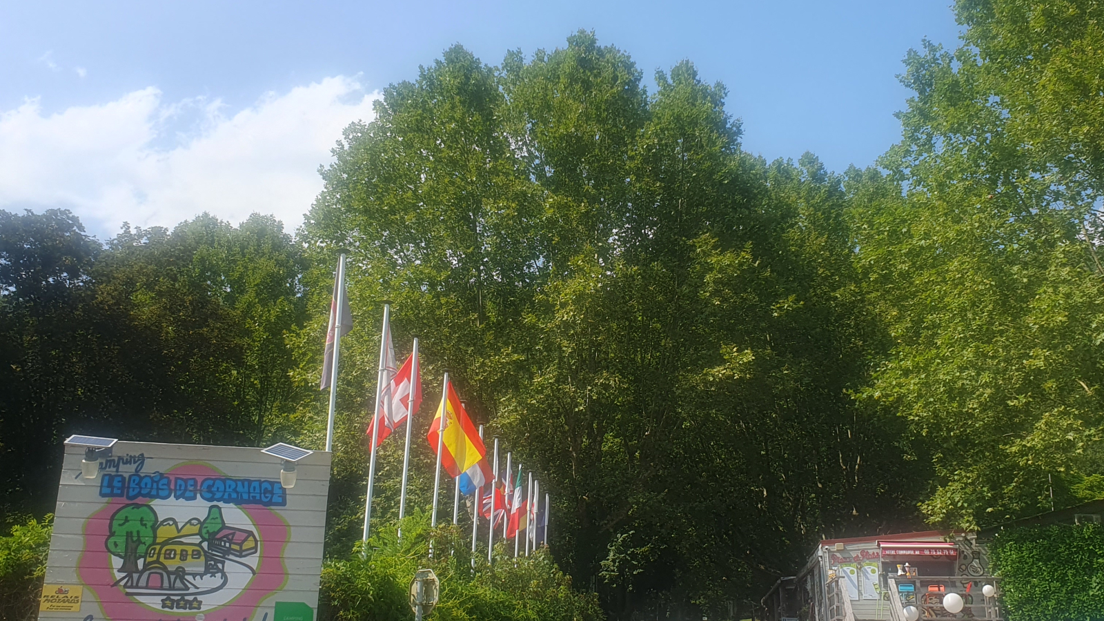 L'entrée du camping est signalée par des panneaux et est accessible par un chemin bordé d'arbres.