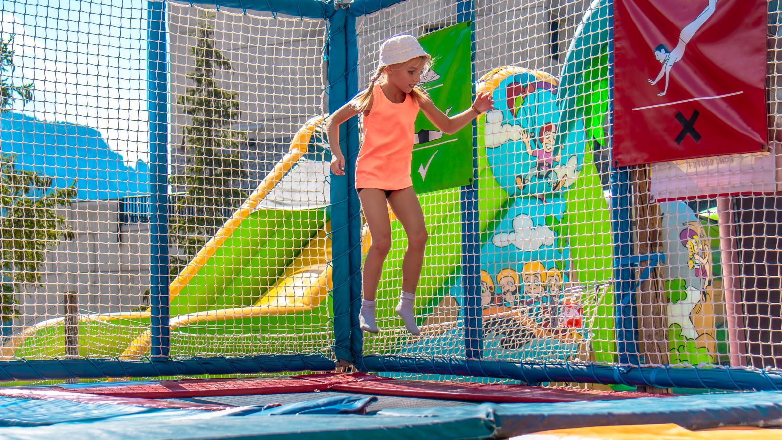 A little girl having fun on a trampoline, with the bouncy castles included in the Flaine Summer Pass in the background