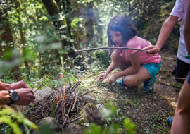 petite fille qui allume un feu de bois en forêt