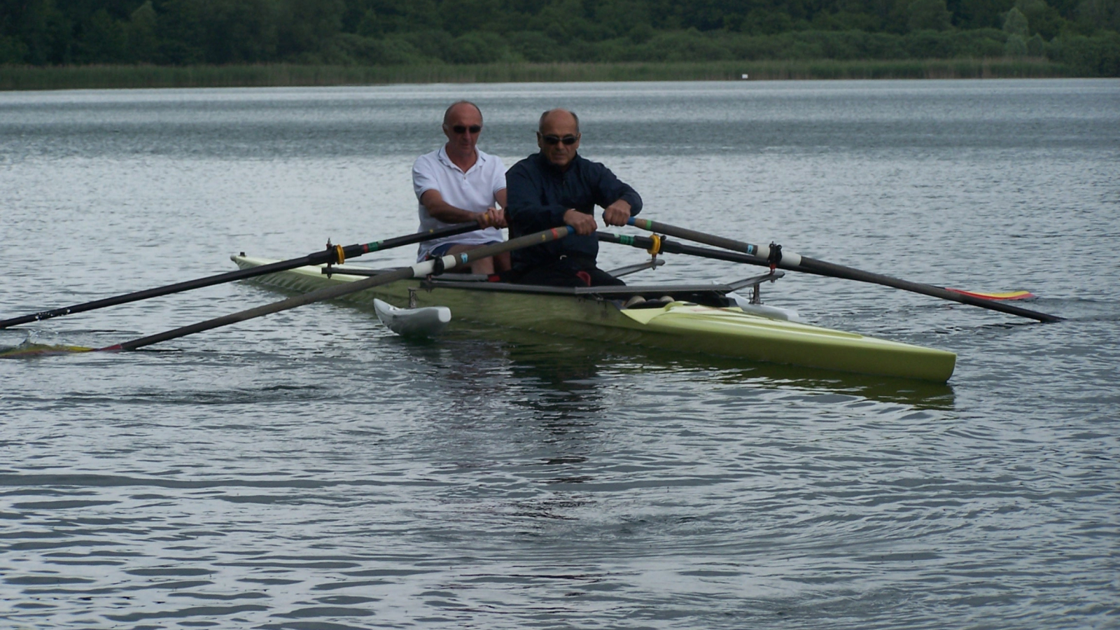 À bord d'un aviron stabilisé sur l'eau, deux personnes rament sur le lac. L'aviron est adapté à l'accueil de deux personnes en situation de handicap.