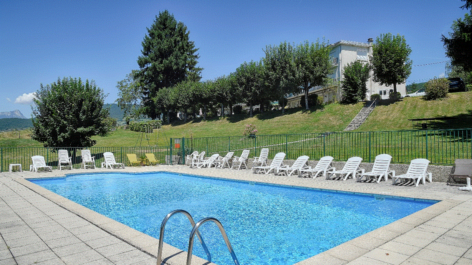 Piscine extérieure rectangulaire, entourée de chaises longues et d'une terrasse ensoleillée.