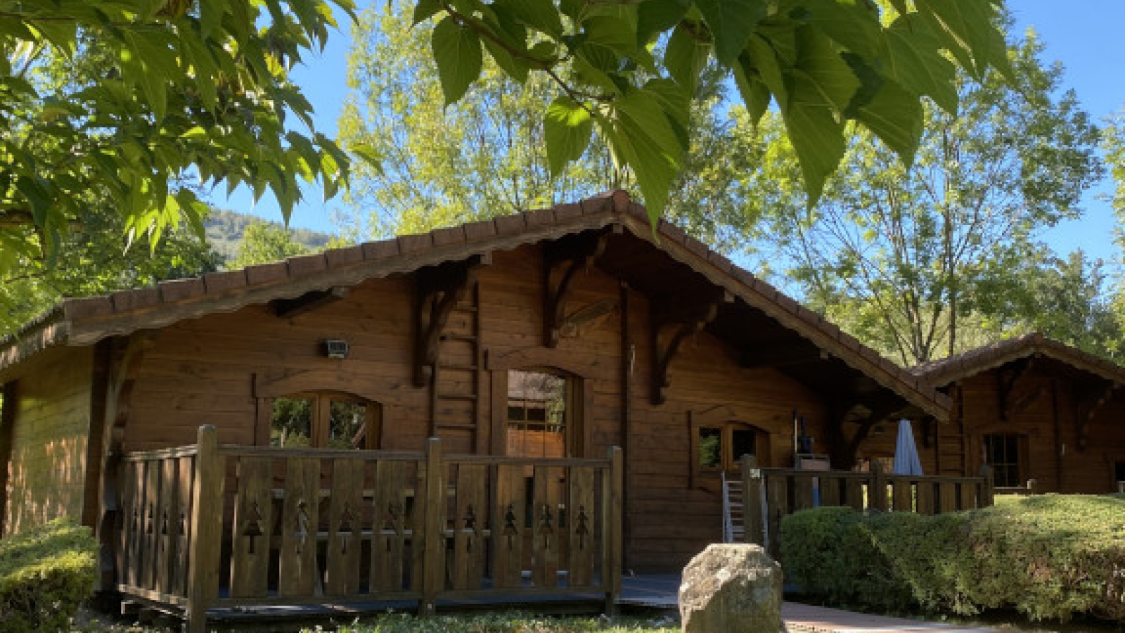 Au premier plan, un chalet en bois, au toit pentu, est niché dans un écrin de verdure. Un deuxième chalet est au second plan.