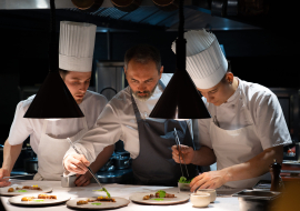 Christophe Aribert préparant un plat entouré de deux cuisiniers