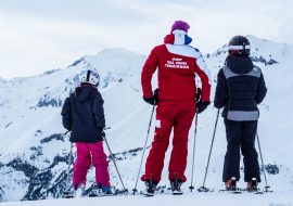 Back view instructor with 2 children on skis