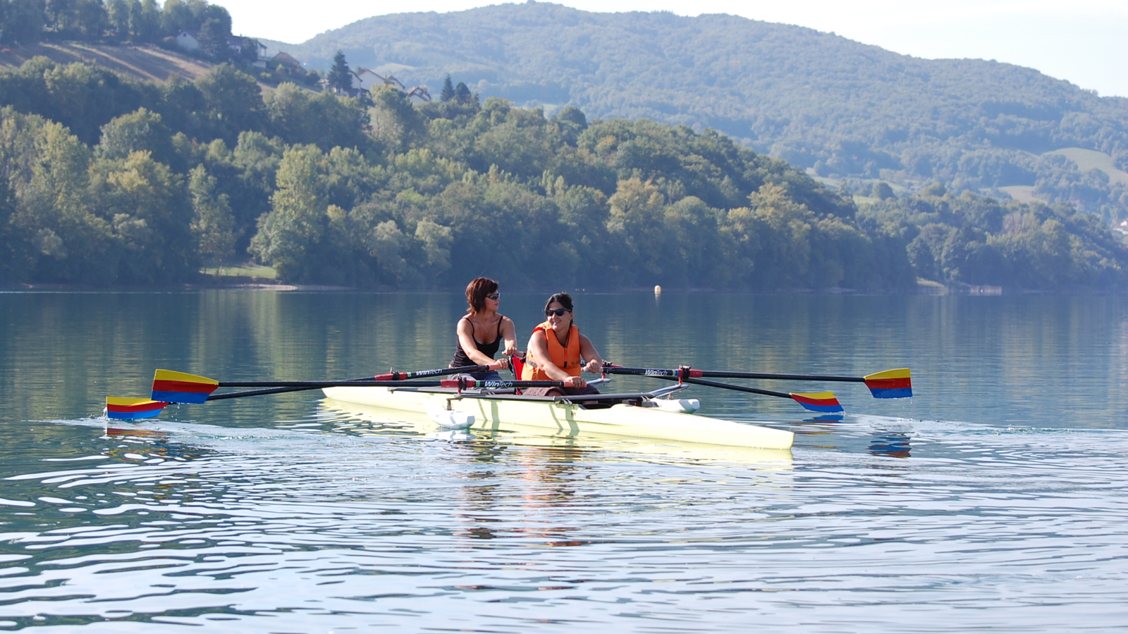 Sous le soleil illuminant le lac et leur passage sur l'eau, deux personnes rament à bord de leur aviron adapté.