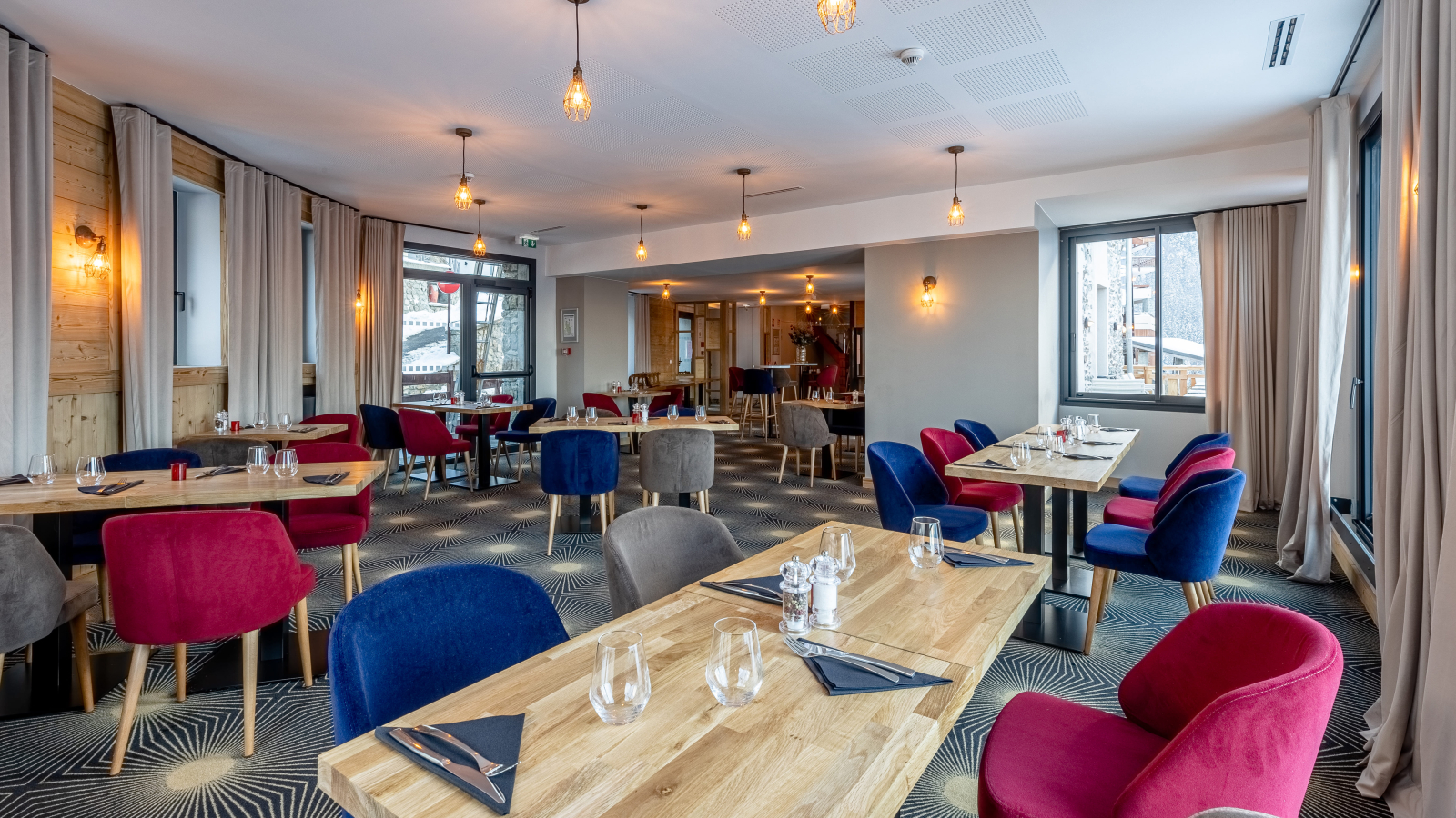 Salle de restaurant avec table en bois et chaises en velours bleue et rouge.